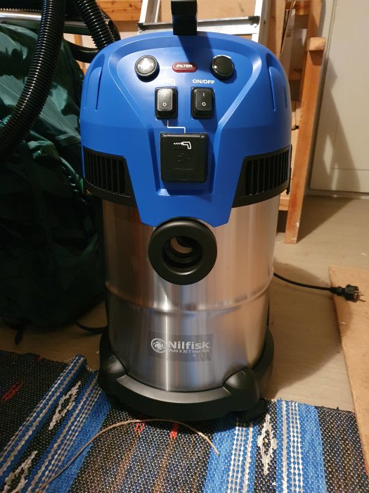 En Nilfisk våt- och torrdammsugare på ett mönstrat golv.
