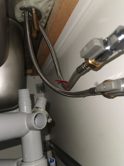 VVS-installation under diskbänk med flexibla slangar och avloppsrör.