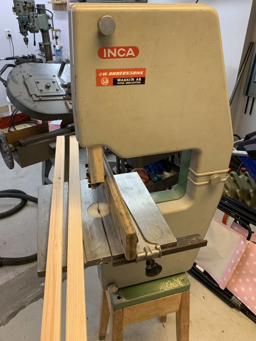 Semi-stationär bandsåg märkt INCA i ett garageverkstad med sågat träemne och annan maskin i bakgrunden.