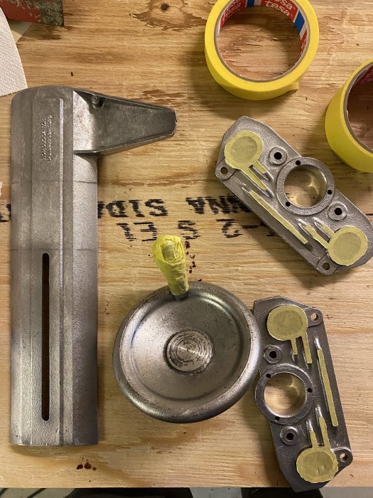 Avrostade och rengjorda metalldelar på ett bord, redo för ommålning, med maskeringstejp i bakgrunden.