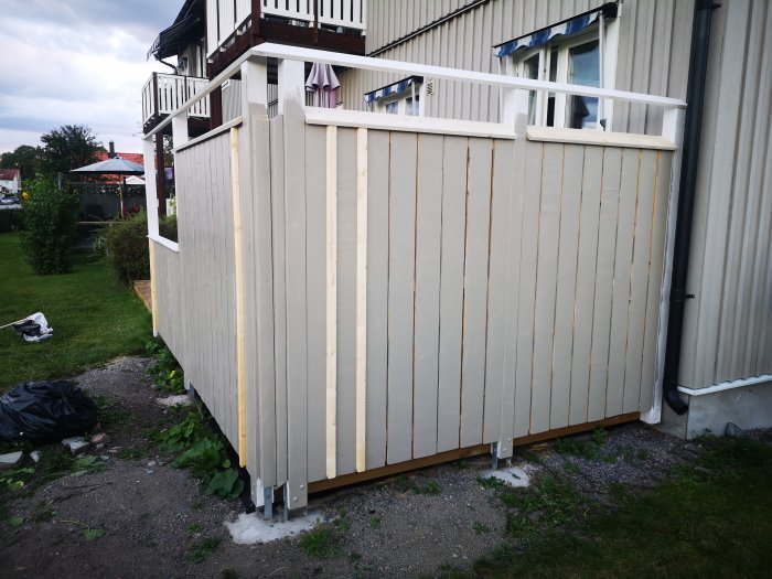 Nybyggt trästaket med täckande färg och osmålade ribbor framför ett hus i skymningen.