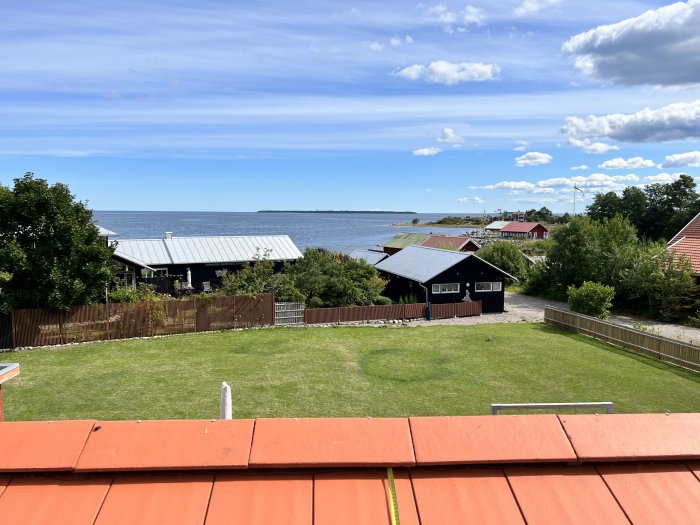 Utsikt från ett tak med nyinstallerad taklucka med en trädgård och havet i bakgrunden.