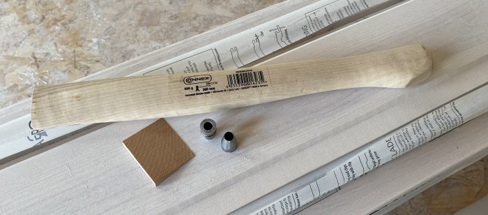 Nytt yxskaft och monteringsdetaljer på ett träbord, redo för renovering av ett yxhuvud.