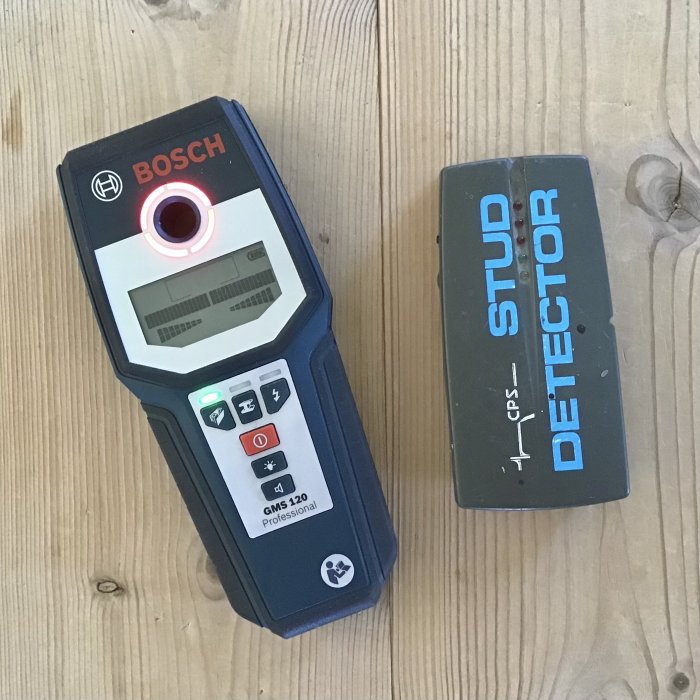 En Bosch GMS120 väggscanner vid sidan av en äldre grå stud detector på ett träbord.