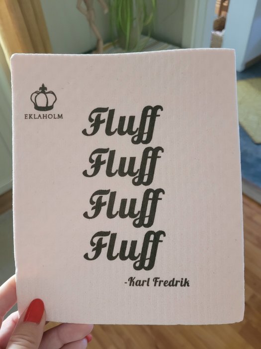 Hand håller en bok med titeln "Fluff" upprepat i svart text, under titeln är "Karl Fredrik" på rosa bakgrund.