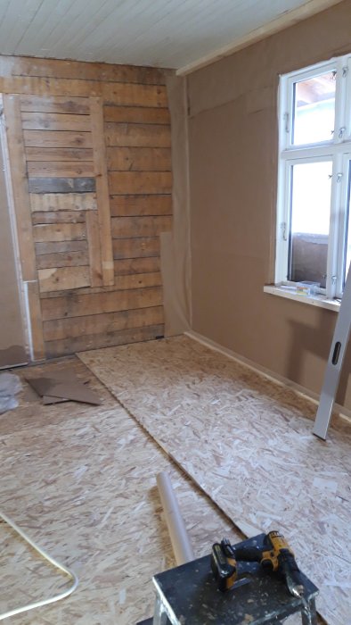 Renoveringsprojekt av ett rum med isolering på vägg, OSB-skivor på golv och verktyg i förgrunden.