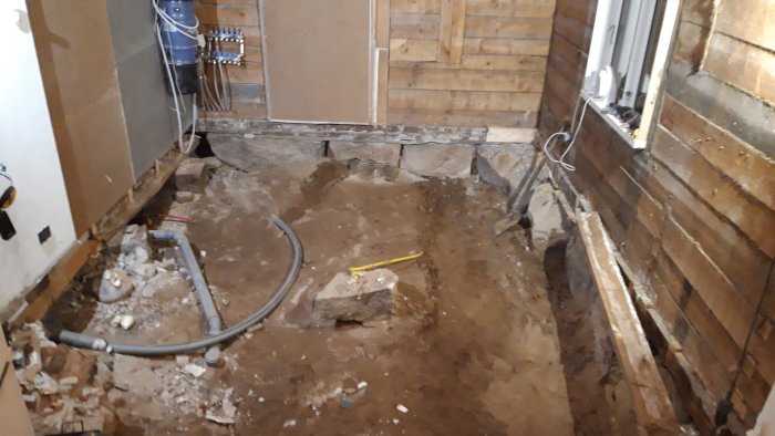 Renoveringsarbete i hus med öppet golv och synliga ledningar, grus och byggmaterial.