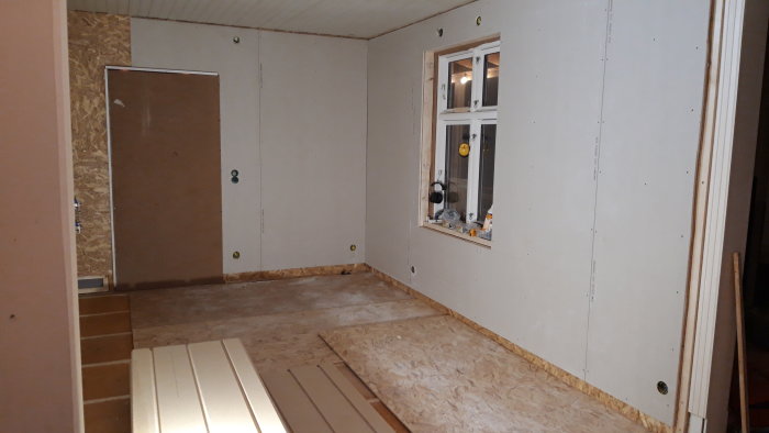 Halvfärdigt rum under renovering med gipsväggar och synliga OSB-skivor.