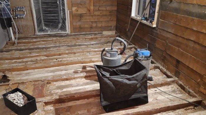 Rippat golv i renoveringsprojekt med synliga bjälkar, verktyg och avfallspåse.