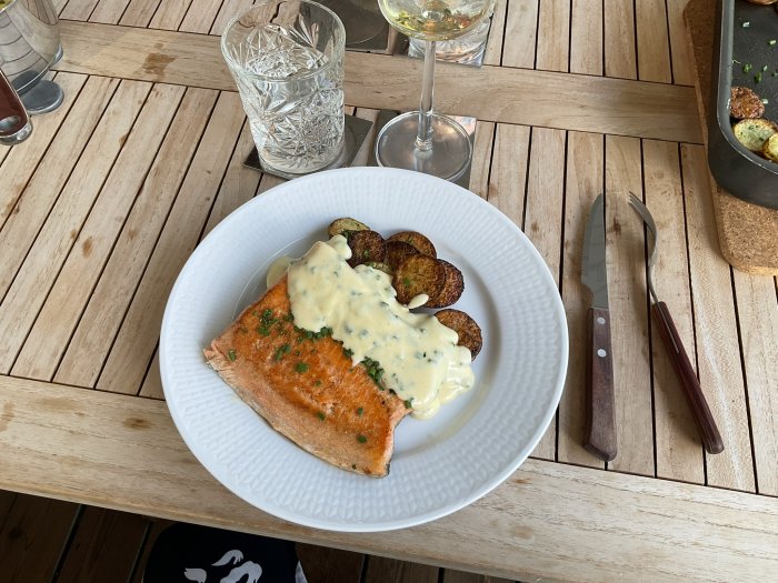 Röding med hollandaisesås ovanpå och dillpotatis på en vit tallrik, kniv och gaffel vid sidan.