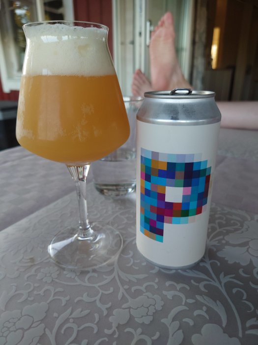 En ölglas fylld med Duckpond DIPA bredvid en ölburk på ett bord, med ofokuserade fötter i bakgrunden.