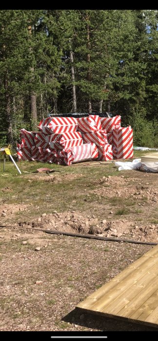 Isoleringsmaterial i rödvita förpackningar staplade i en skogsglänta med träplankor i förgrunden.