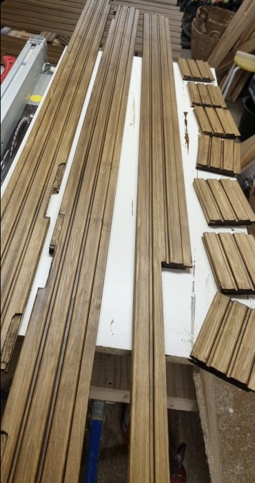 Flera träprofiler och lister i olika längder och former, bearbetade och oljade för dörrmontering, ligger på ett arbetsbord.