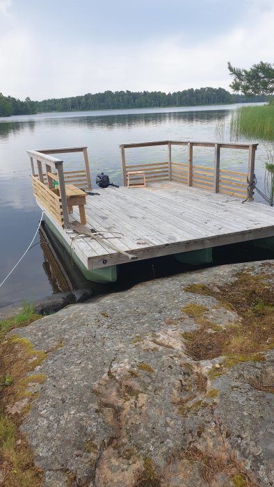 En nybyggd flotte med träreglar och räcken flyter vid sjöns strandkant.