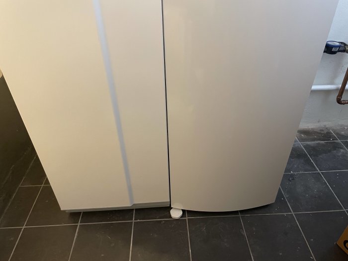 Varmvattenberedare i hörn av rum med synliga rör och en del av golvet.