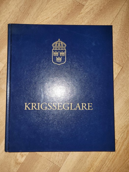 Blå bok med titeln KRIGSSEGLARE och förlagsmärke på en träyta.