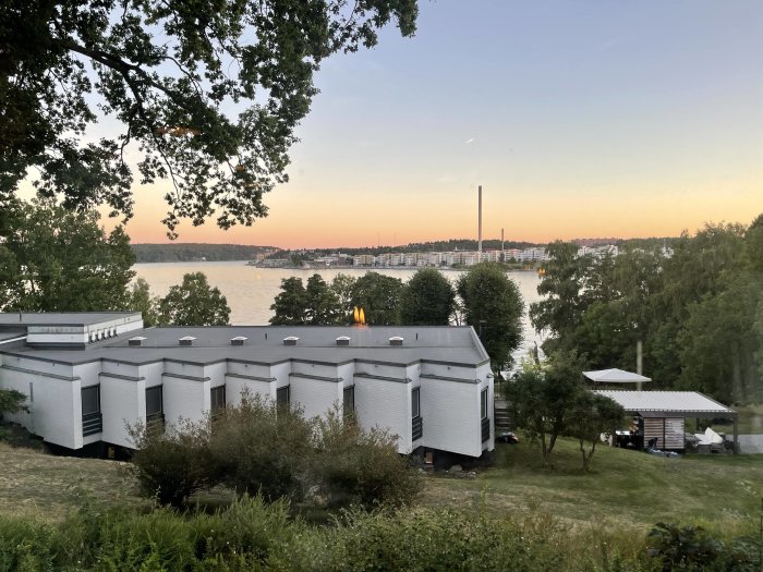 Utsikt över vit byggnad och trädgård med utsikt över vatten och stad i skymningen från Lidingö.