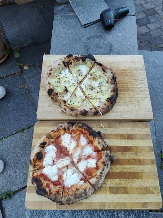 Två hembakade pizzor på skärbrädor med bakgårdsstenar och ett mätverktyg i bakgrunden.