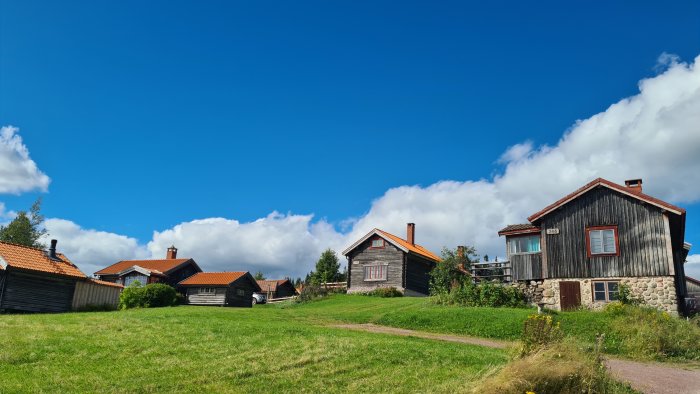 Traditionella svenska trähus i en lantlig miljö med klarblå himmel och vita moln.