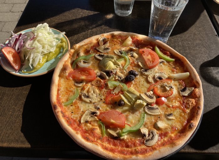 Vegetarisk pizza med tomat, paprika, champinjoner och lök serverad med sallad och vatten.