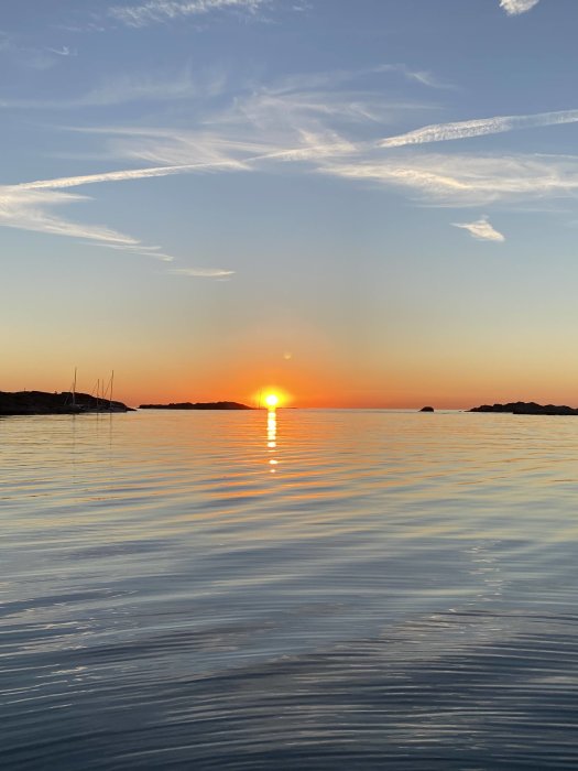 Solnedgång vid kusten med klippor och reflektion över lugnt hav.