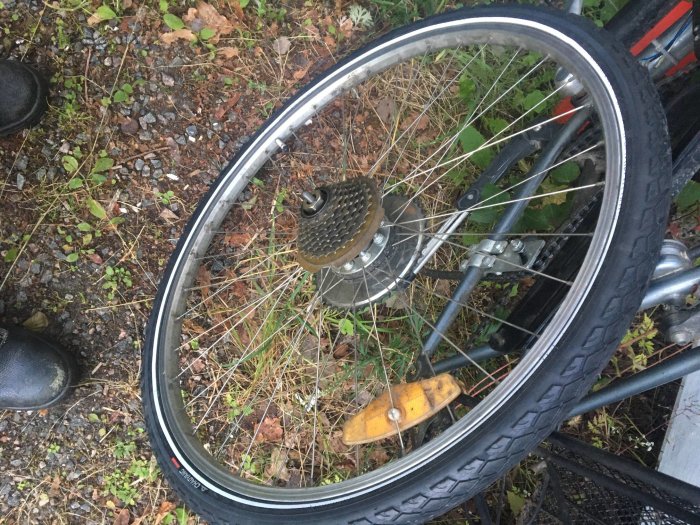 Cykelhjul med platt däck och kassett mot grusig mark och grönska.