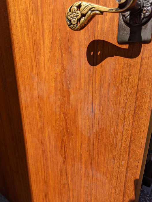 En träytterdörr i solen med fokus på en gammaldags, detaljerad dörrhandtag i metall.