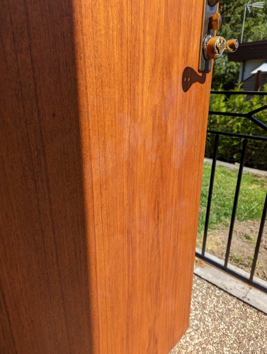 Solbelyst träytterdörr med gyllene dörrhandtag och skugga av ett dörrstopp på en solig dag.