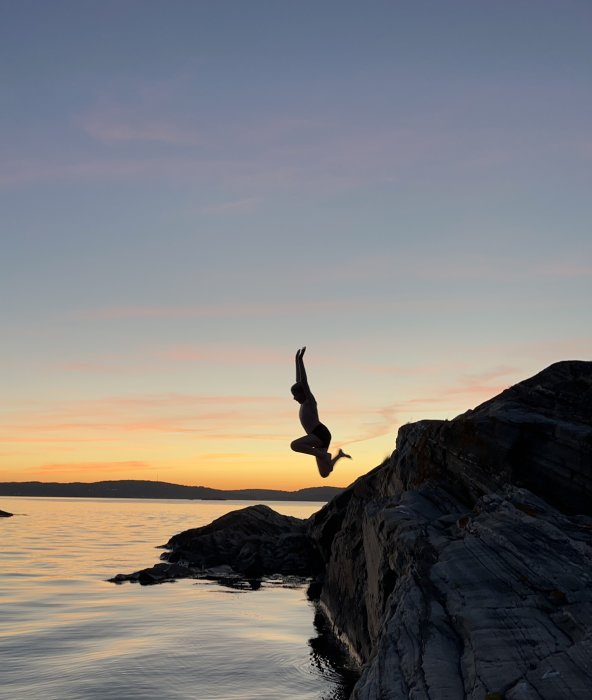 Person utför ett hopp från en klippa vid solnedgång över havet.