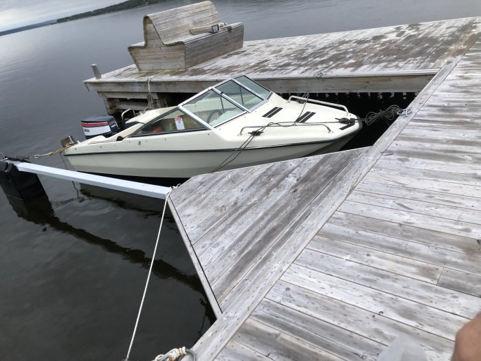 Motorbåt förtöjd vid en träbrygga på ett lugnt vatten.