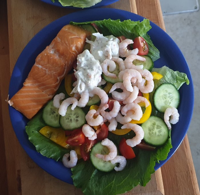 Räkor och laxfilé på en bädd av krispig sallad med gurka, tomat och dressing, en lågkolhydratmåltid.