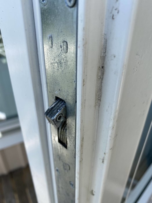 Närbild på en vit dörr och metallplåt med ett utskjutande metallbeslag som ser ut att vara skadat eller felmonterat.