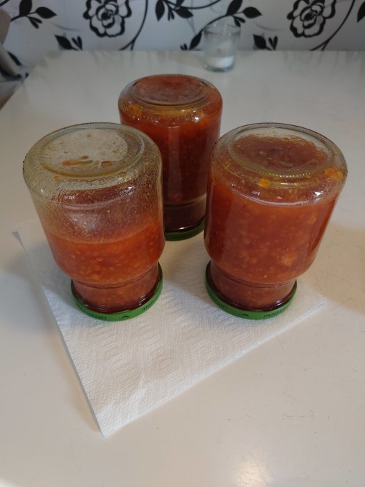 Tre glasburkar med hembakt tomatsås på ett köksbord.