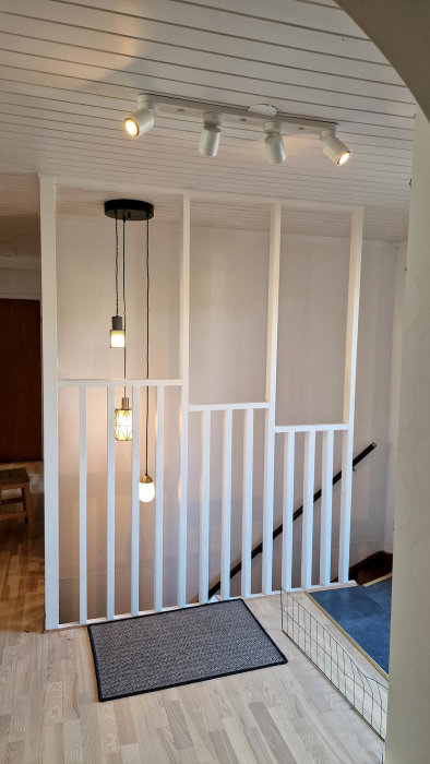 Interiörbild av en trappa med vita stolpar och upphängda taklampor av olika stilar.