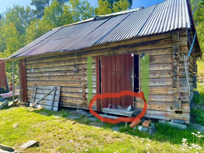 Gammal timmerstuga med sjöbleckstak och en markerad trasig trappa på framsidan.