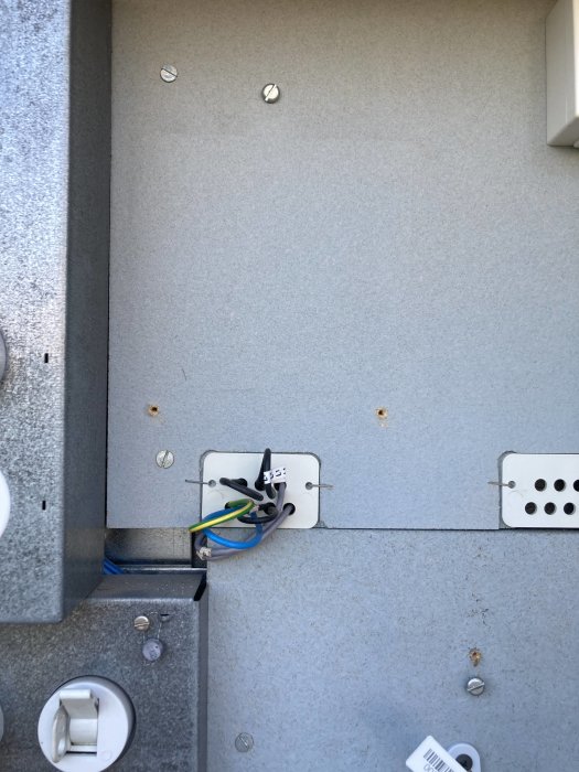 Eluttag under installation med synliga kablar och monteringsplatta på en grå vägg.
