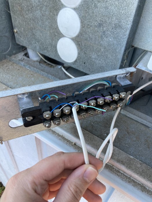 Hand som håller en vit elsladd kopplad till en kabelskena med flera färgade kablar vid en byggnadsinstallation.