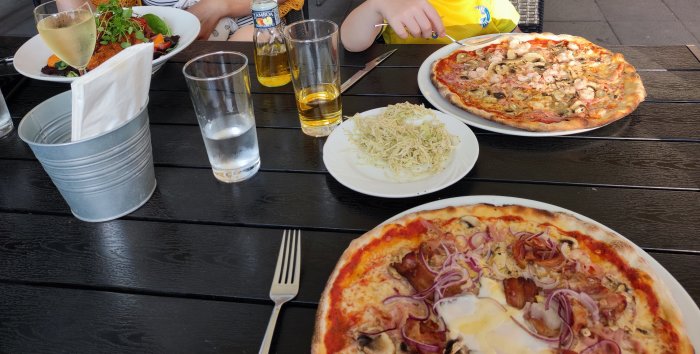 Middag utomhus med olika pizzor och en salladstallrik på ett svart träbord.