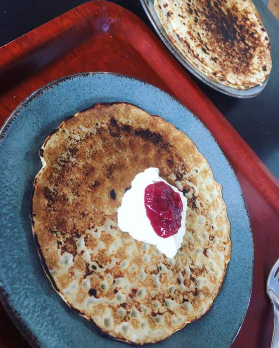 Pannkaka med grädde och sylt på blått fat framför en annan pannkaka på rött fat.