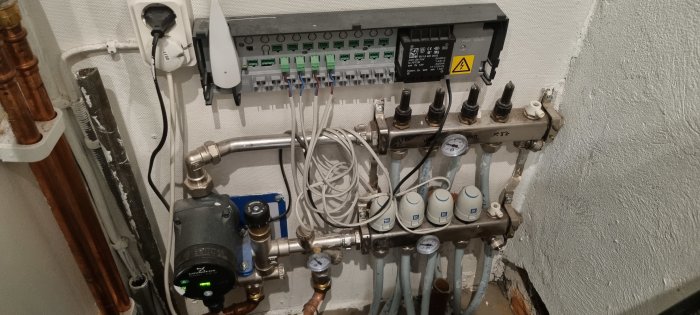 Installation av uppvärmningssystem med rör, manometer och en elektrisk centralenhet på en vägg.