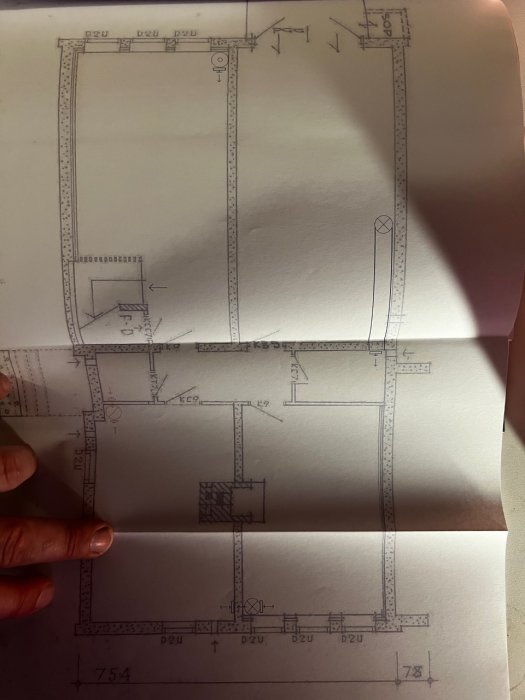 Hand som håller en skiss med ritningar av byggprojekt som visar rördragning och planlösning.