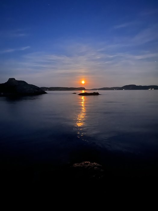 Månsken reflekterande över havet med silhuett av klippor och stjärnhimmel.