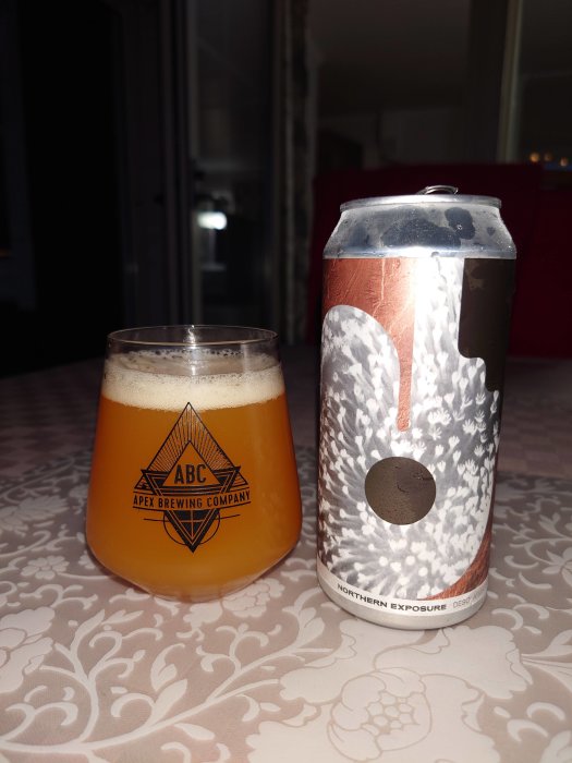 DIPA-öl i glas bredvid burken på mönstrat bord, Apex Brewing Company-logotyp synlig.