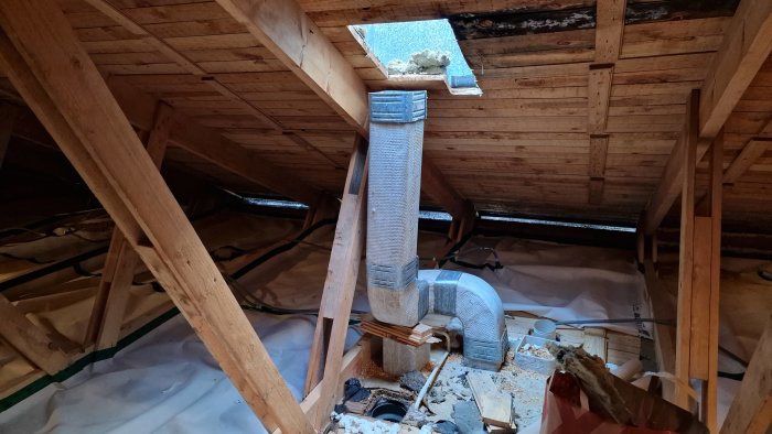 Ventilationsrör och böjar vid takgenomföring i ett rörigt vindsutrymme med isolering och träreglar.