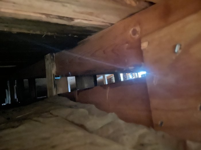 Trång vinkel av vindgavel i hus visar isolering och träbjälkar med ljusinsläpp för ventilation.