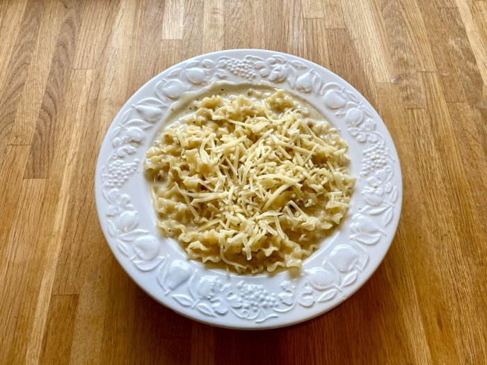 Carbonara med riven texmex ost på en vit tallrik mot träbordsbakgrund.