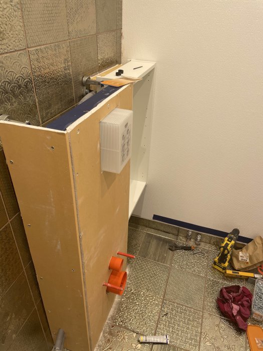 Badrum under renovering med kaklade väggar och installerade vägghängda toalettstommen, verktyg på golvet.