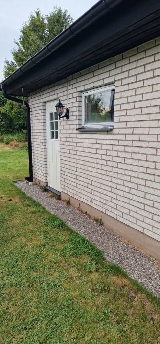 Utsidan av en garageutbyggnad med tegelklädsel och takskarv, inklusive en vit dörr och fönster.