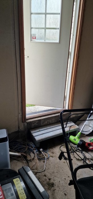 Dörröppning med skarv i garaget, steg och kablarna på golvet, med byggbråte runtomkring.
