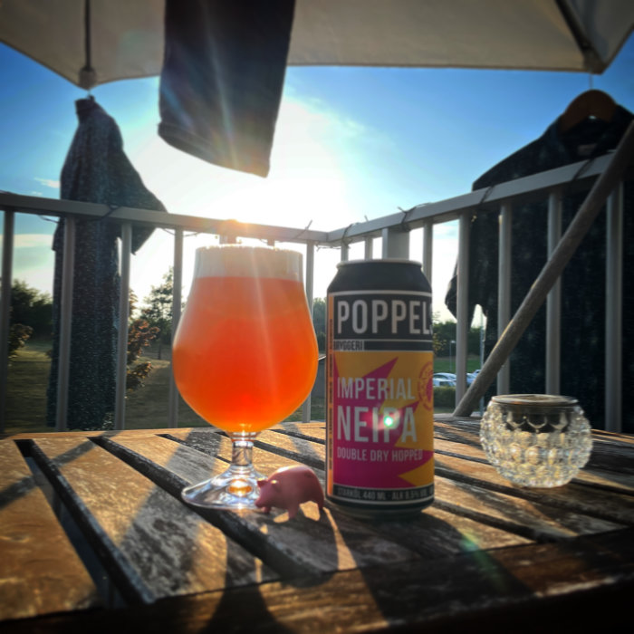 Ölglas och burk med Imperial NEIPA på bord i solnedgång, tvätt hänger på tork i bakgrunden.
